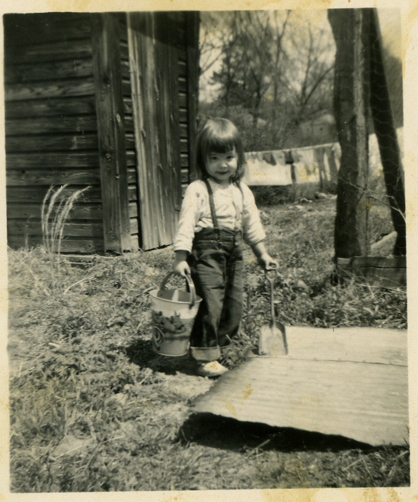 A little girl with bangs holding a bucket and a shovel